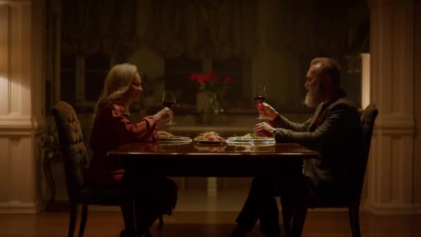 Amor pareja de ancianos tintineo vasos de vino y hacer tostadas en la mesa de casa. Retiro — Vídeo de stock