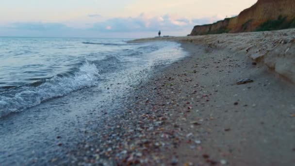 Fale morskie woda rozpryskująca piasek o wschodzie słońca. Samotna kobieta spacerująca po plaży — Wideo stockowe