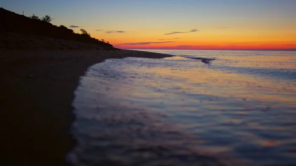 オレンジ色の日没の夜明けに岩の海岸。暗い砂浜で穏やかな海の景色 — ストック写真