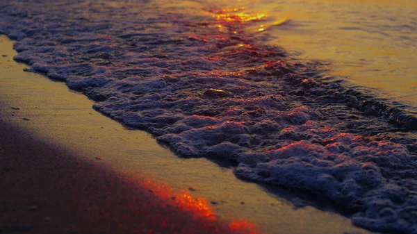 Primer plano olas de mar salpicando playa de arena en cámara lenta puesta de sol naranja noche — Foto de Stock