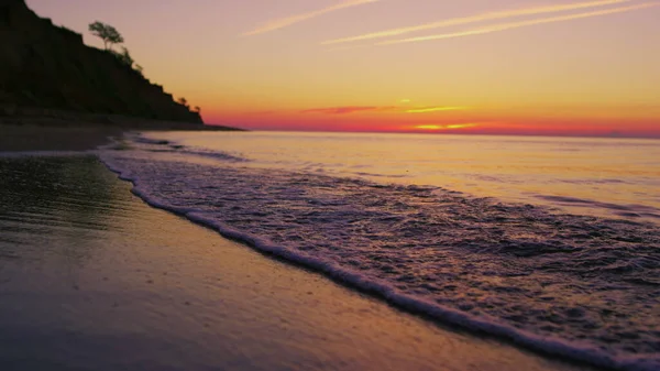 Tranquillo litorale oceanico con colline di montagna silhouette al tramonto arancione brillante — Foto Stock