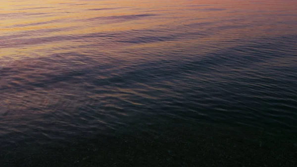 Primer plano calma océano agua superficie reflejando brillante rosa amanecer cielo por la mañana — Foto de Stock