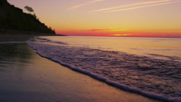 Friedliche Meeresküste mit Berghügelsilhouette bei leuchtend orangefarbenem Sonnenuntergang — Stockvideo