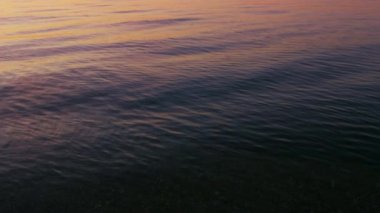 Yakın çekim sakin okyanus yüzeyi parlak pembe gündoğumu gökyüzünü yansıtıyor.