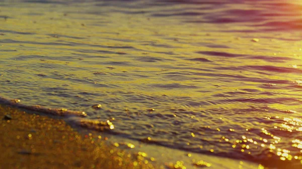 Onde marine spruzzando spiaggia di sabbia dorata. Superficie dell'acqua riflettente tramonto giallo — Foto Stock
