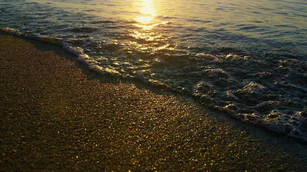 Отражение солнечного света в морских волнах, плескающихся пляжным песком на золотом восходе солнца — стоковое фото
