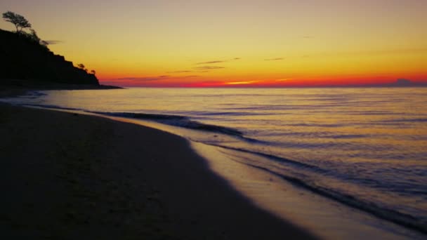Côte du lac à l'aube du coucher du soleil orange. Plage de mer sombre avec silhouette de montagne — Video