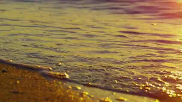 Ondas do mar salpicando praia de areia dourada. Superfície da água refletindo o pôr do sol amarelo — Vídeo de Stock