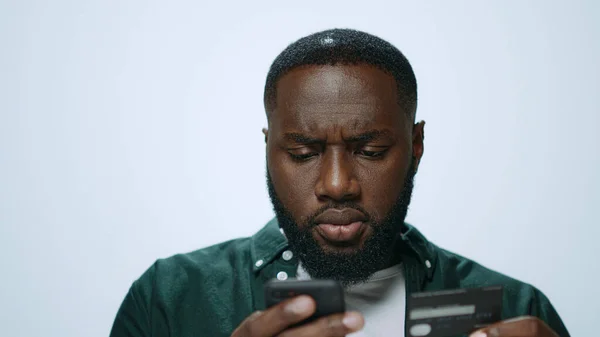 Konzentrierter Afrikaner kauft im Studio erfolgreich online auf Smartphone ein. — Stockfoto
