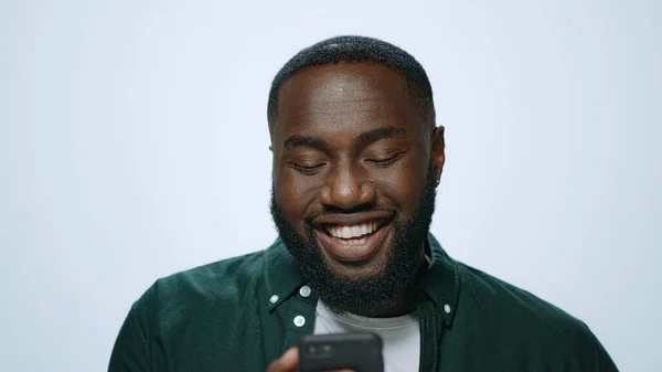 Nahaufnahme glücklicher afrikanischer Mann, der im Studio auf seinem Handy im Internet surft. — Stockfoto