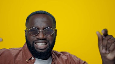 Güneş gözlüklü neşeli Afrikalı Amerikalı adam sarı arka planda dans ediyor..