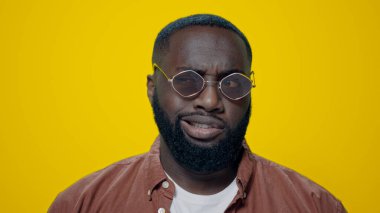 Sarı arka planda komik suratlar yapan afro yakışıklı bir adam portresi.