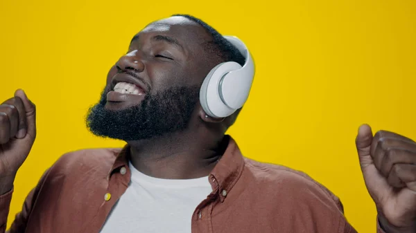 Portrait of happy african man dancing in headphones on yellow background.