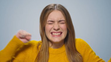 Gri arka planda zaferin keyfini çıkaran olumlu kadın portresi.