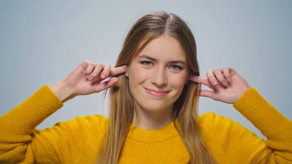 Portret van een lachende vrouw bedekt haar oren met vingers op camera in de studio. — Stockfoto