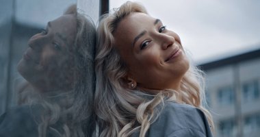 Şehir mimarisinde sarışın saçlarıyla gülümseyen güzel bir kadın..