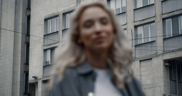 Блондинка улыбается городскому пейзажу возле зданий на размытом фоне — стоковое фото