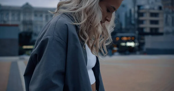 Blonde woman looking down in evening city urban background.