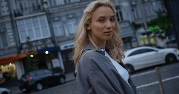 Blondes weibliches Model läuft in Abendstadt nahe Straße mit fahrendem Auto. — Stockfoto