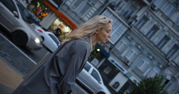 평온 한 여자가 지나가는 차를 가지고 저녁에 시내 길을 걷고 있다. — 스톡 사진
