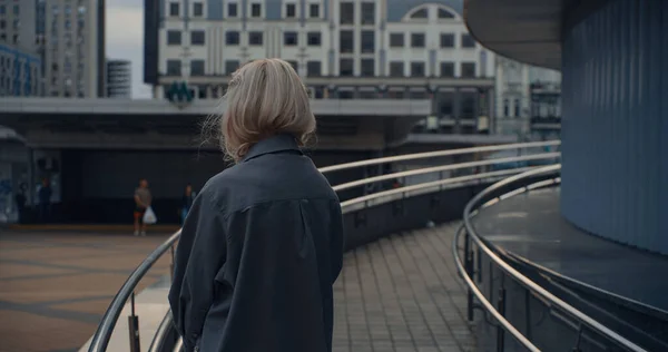 금발 소녀 는 도시 건물 근처에서 누군가를기다리는 도시를 바라본다. — 스톡 사진