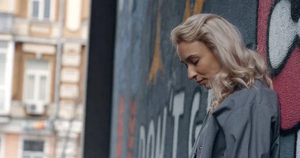 Femme blonde regardant la ville près du mur de graffiti sur le bâtiment urbain. — Photo