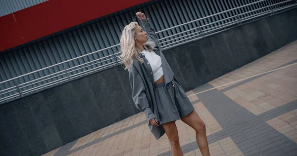 Modelo atraente fazendo movimentos com cabelo loiro perto da cidade edifício moderno. — Fotografia de Stock