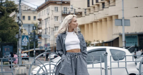 Блондинка позирует городским зданиям на дороге с проезжающими автомобилями. — стоковое фото