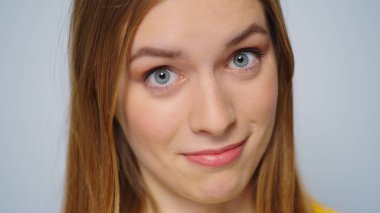 Yakın plan, gri arka planda kameraya gülümseyen kadını şaşırttı. Komik kız yüzü. 