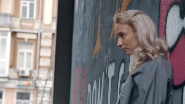Ξανθιά γυναίκα ψάχνει την πόλη άποψη κοντά στον τοίχο γκράφιτι στο αστικό κτίριο. — Αρχείο Βίντεο