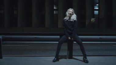 Gülen kadın gece karayolu. Kentin karanlık yolundaki bankta otururken..