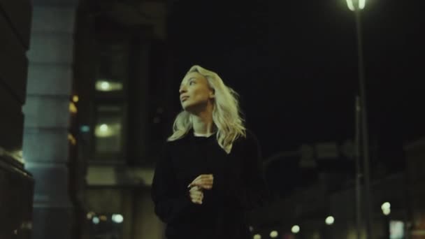 Blondýny žena chůze noc sama v městském oblečení v moderním městě. — Stock video