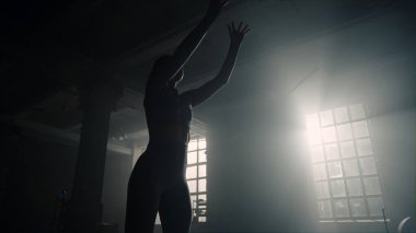 Spor salonunda tıp topuyla çömelme yapan bir kız. Duvara top atan kadın