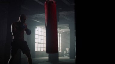 Eldivenle kum torbasına vuran bir sporcu. Spor çantasına yumruk atan bir adam. 