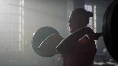 Adam halterle çömelme hareketi yapıyor. Ağır ağırlıklarla vücut geliştirme sporu 