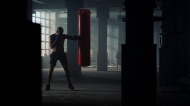 Boksör tavan arasında spor çantasına yumruk atıyor. Yumruk torbasını eldivenle tekmeleyen adam