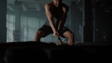 Lastiğe çekiçle vuran bir adam. Atletik sporcu güç egzersizi yapıyor.