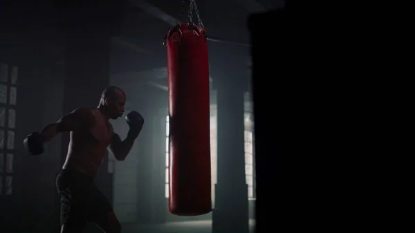 Hombre afroamericano boxeando saco de boxeo en gimnasio. Sportsman perforando bolsa de deporte — Foto de Stock