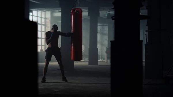 Fighter stansning sportväska i loft byggnad. Man sparkar boxningssäck i handskar — Stockfoto