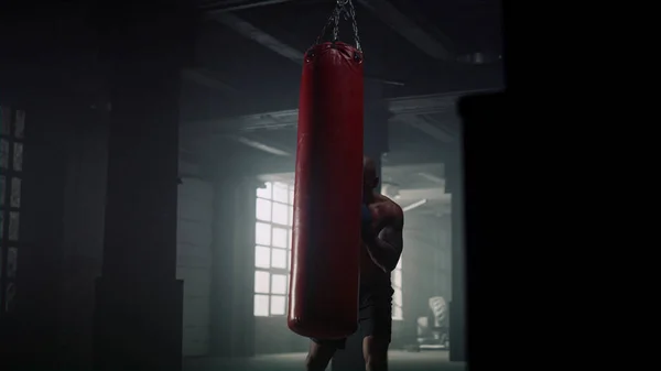 Athletic sportsman boxing punch bag in sport club. Guy training boxing in gym