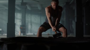 Büyük lastikleri çekiçle döven odaklanmış bir adam. Balyoz kullanan vücut geliştirici 