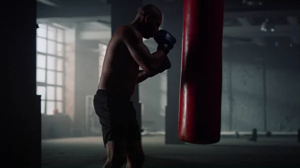 Hombre saco de boxeo en el club deportivo. Tipo agresivo patadas bolsa de deporte — Foto de Stock