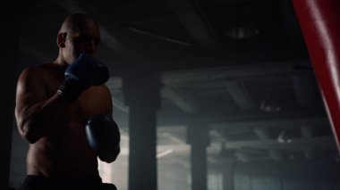 Çatı katında boks eğitimi alan bir adam. Erkek dövüşçü kum torbasını tekmeliyor 