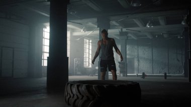 Spor salonunda lastik patlatan bir adam. Erkek atlet ağır lastik lastiği kaldırıyor