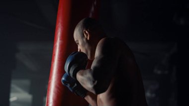 Spor kulübünde boks antrenmanı yapan bir adam. Adam antrenman sırasında kum torbası tekmeliyor.