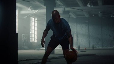 Basketbolcu spor kulübünde top sektiriyor. Sporcu spor salonunda top sürüyor.