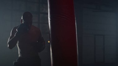 Kum torbasıyla boks antrenmanı yapan adam. Sporcu spor çantasına yumruk atıyor.