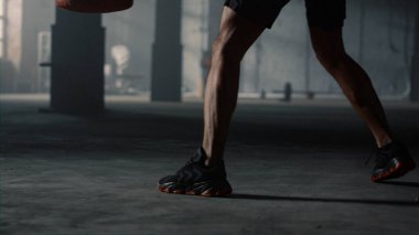 Boks antrenmanı sırasında erkek bacakları hareket ediyor. Kickboks antrenmanı yapan adam kum torbasıyla