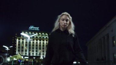 Kentin arka planında, gece sokak lambalarında yürüyen kendinden emin bir kız.. 