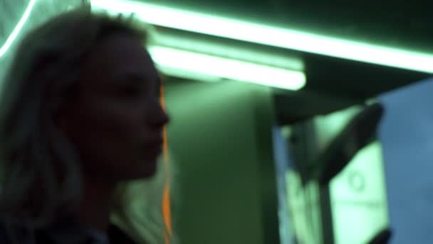 Blond meisje modelleren blik aanraken haar in neon lichten stad achtergrond. — Stockvideo